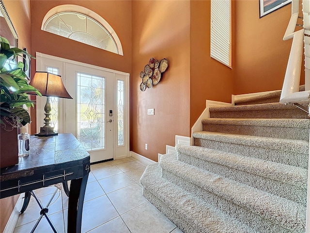 entryway with light tile patterned floors, a high ceiling, stairs, and baseboards