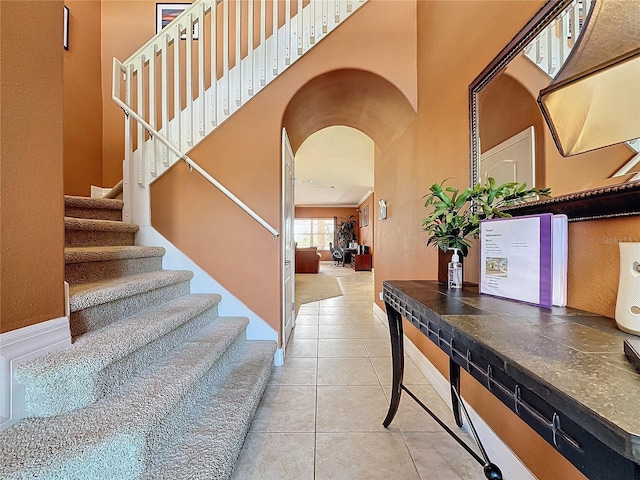 stairs featuring tile patterned flooring, baseboards, arched walkways, and a towering ceiling