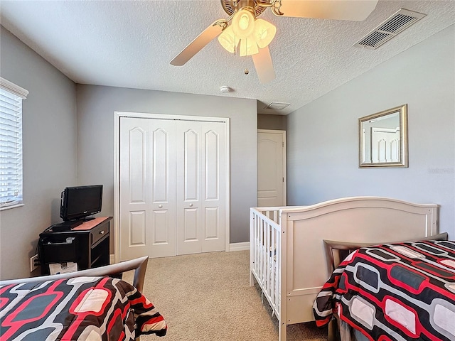 carpeted bedroom featuring visible vents, a textured ceiling, a closet, and ceiling fan