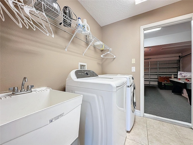 washroom with a sink, a textured ceiling, light tile patterned flooring, a garage, and washing machine and clothes dryer