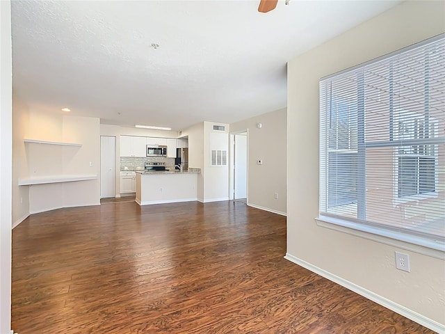 unfurnished living room featuring visible vents, a ceiling fan, dark wood-style flooring, and baseboards