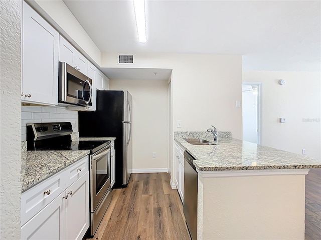 kitchen with visible vents, light wood finished floors, a peninsula, a sink, and stainless steel appliances