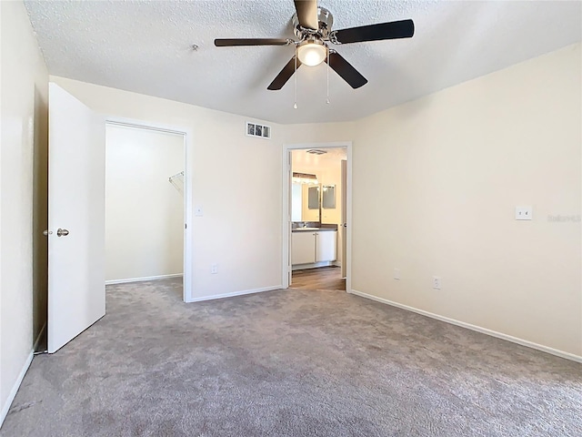 unfurnished bedroom with a walk in closet, carpet, visible vents, and a textured ceiling