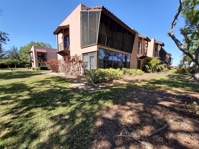 rear view of house with a balcony, a lawn, and stucco siding