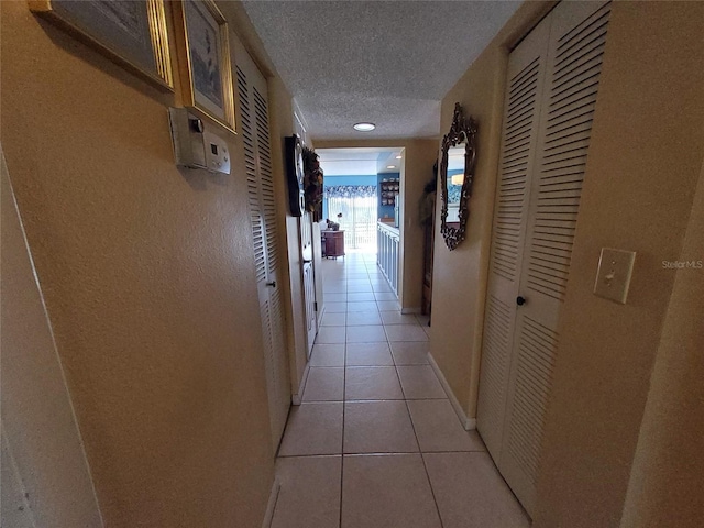 hallway with light tile patterned floors, a textured ceiling, and baseboards