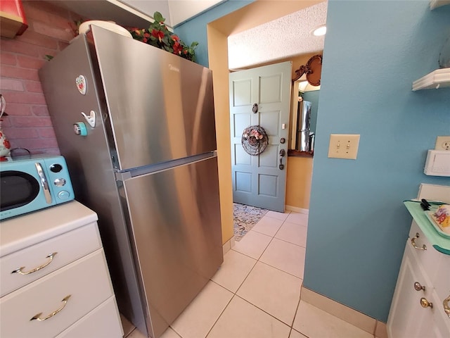 kitchen with light tile patterned flooring, a textured ceiling, white cabinetry, and freestanding refrigerator