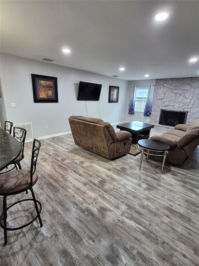 living room featuring visible vents, baseboards, a stone fireplace, recessed lighting, and wood finished floors