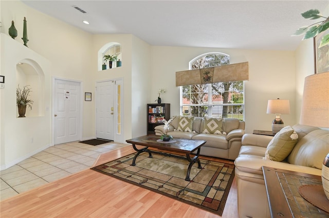 living area featuring light wood-style flooring, baseboards, visible vents, and high vaulted ceiling