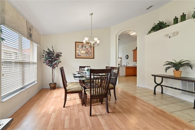 dining space with visible vents, baseboards, light wood-style floors, arched walkways, and a notable chandelier