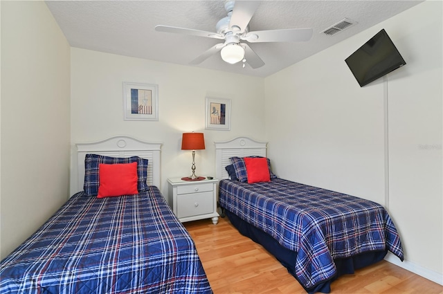 bedroom with ceiling fan, visible vents, a textured ceiling, and wood finished floors