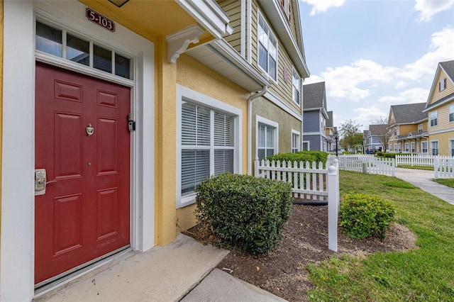 view of exterior entry featuring a residential view, stucco siding, and fence