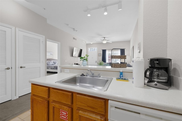 kitchen featuring dishwasher, light countertops, brown cabinets, a ceiling fan, and a sink