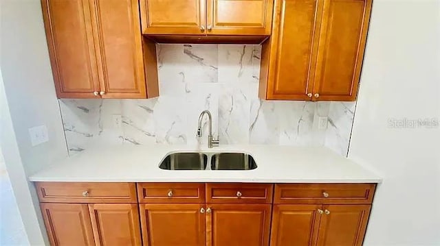 kitchen with tasteful backsplash, brown cabinetry, light countertops, and a sink