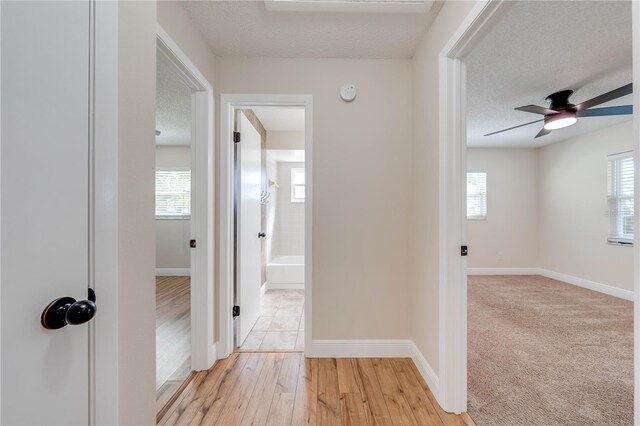 corridor featuring baseboards, a textured ceiling, and light wood-style floors