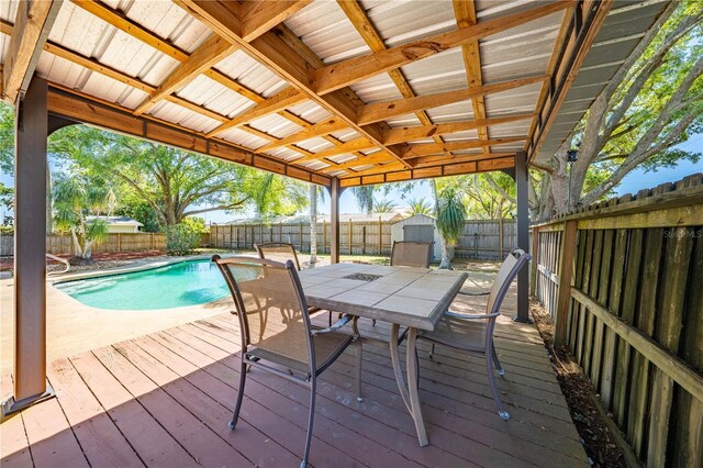 wooden deck featuring an outbuilding, a fenced in pool, outdoor dining area, a fenced backyard, and a storage shed