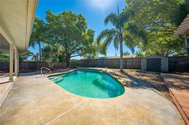 view of pool with an outbuilding, a storage shed, a fenced backyard, and a patio area