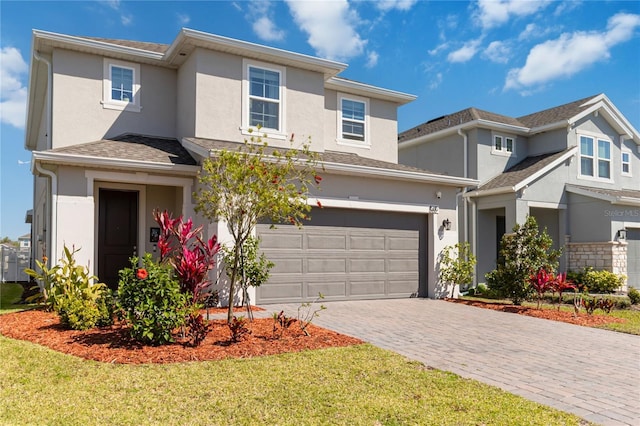 traditional-style home with stucco siding, decorative driveway, roof with shingles, a front yard, and an attached garage