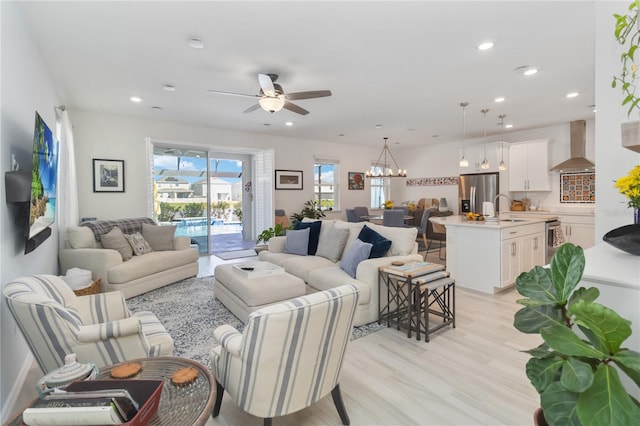 living room featuring light wood finished floors, recessed lighting, and ceiling fan with notable chandelier