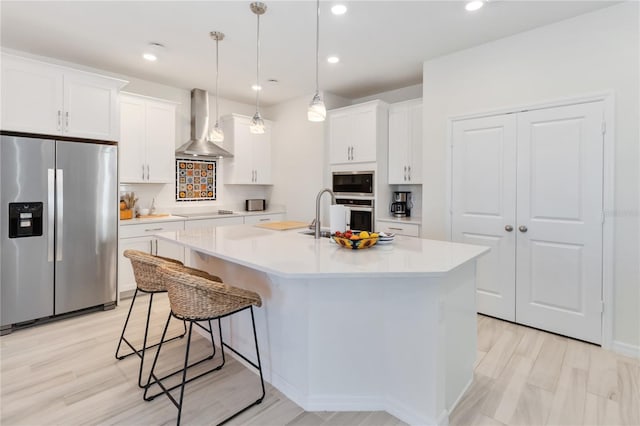 kitchen featuring wall chimney range hood, light countertops, a kitchen breakfast bar, appliances with stainless steel finishes, and white cabinetry