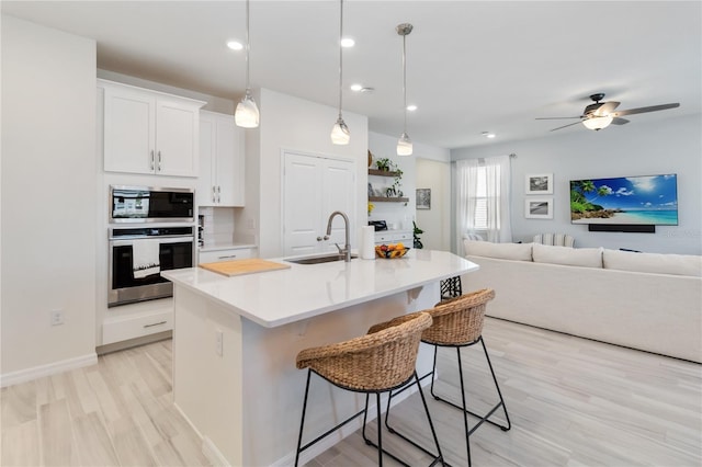 kitchen with a sink, open floor plan, appliances with stainless steel finishes, a breakfast bar area, and light countertops