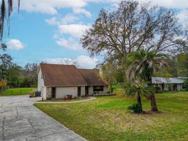 view of front facade with cooling unit, fence, concrete driveway, a front lawn, and a garage