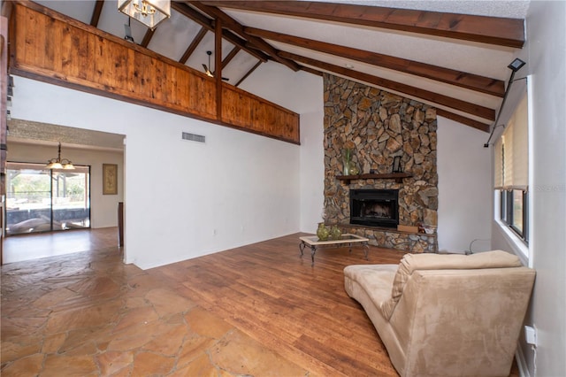 living area with visible vents, beam ceiling, high vaulted ceiling, wood finished floors, and a stone fireplace