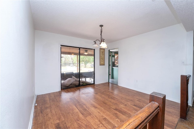 empty room with baseboards, a notable chandelier, wood finished floors, and a textured ceiling