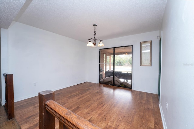 spare room with baseboards, a notable chandelier, wood finished floors, and a textured ceiling