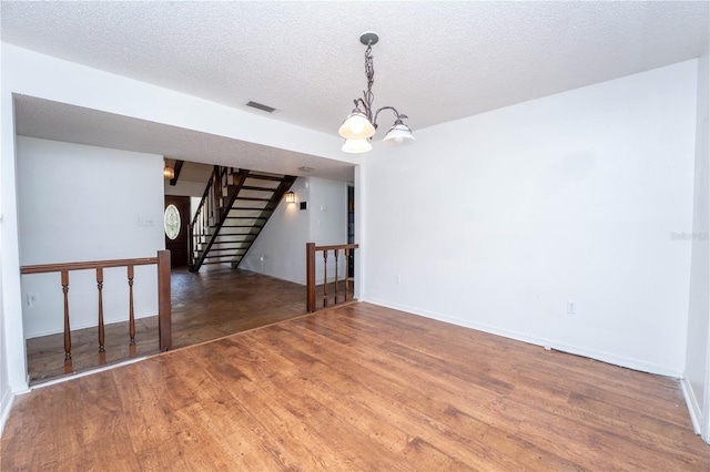 empty room featuring visible vents, a textured ceiling, wood finished floors, a chandelier, and stairs