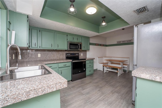 kitchen featuring a tray ceiling, visible vents, green cabinetry, and stainless steel appliances