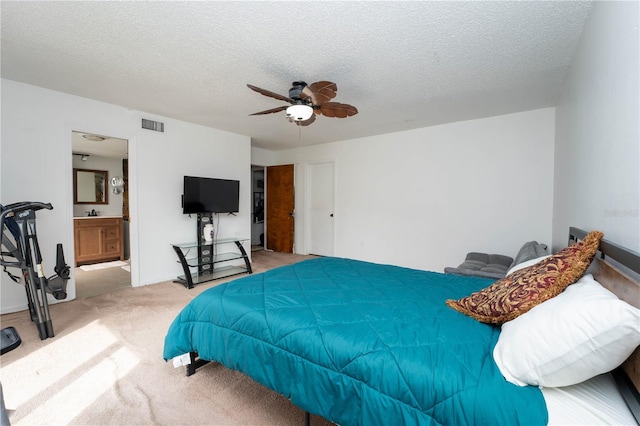 carpeted bedroom with visible vents, ensuite bathroom, a textured ceiling, and a ceiling fan