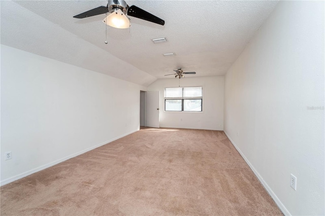 empty room with baseboards, ceiling fan, light colored carpet, vaulted ceiling, and a textured ceiling