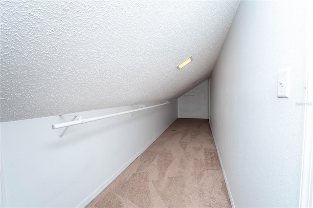 interior space featuring lofted ceiling, light colored carpet, baseboards, and a textured ceiling