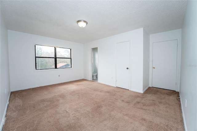 unfurnished bedroom featuring ensuite bath, a textured ceiling, baseboards, and carpet floors