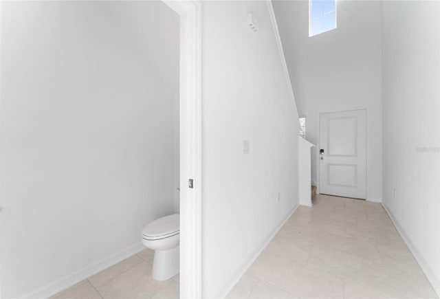 bathroom featuring tile patterned floors, a high ceiling, toilet, and baseboards