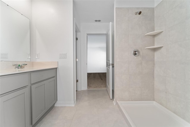 bathroom featuring visible vents, baseboards, tiled shower, tile patterned floors, and vanity