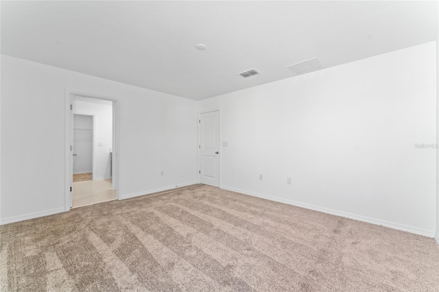 unfurnished room with visible vents, light colored carpet, and baseboards