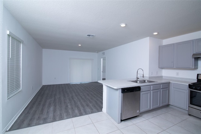 kitchen with gray cabinetry, open floor plan, a peninsula, stainless steel appliances, and a sink