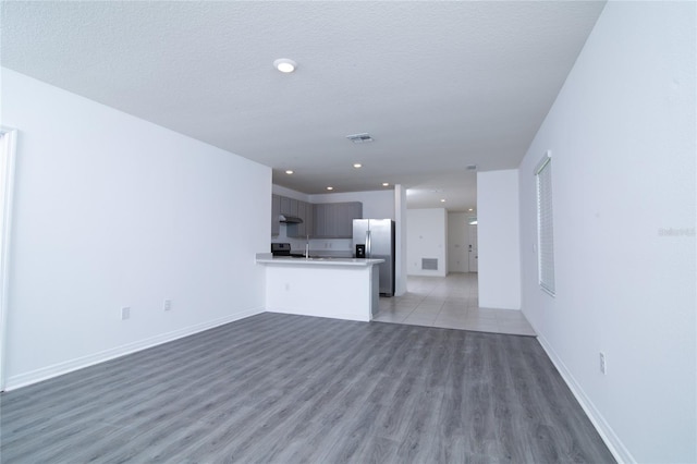 unfurnished living room with visible vents, a textured ceiling, recessed lighting, light wood-style floors, and baseboards