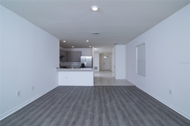 unfurnished living room featuring a textured ceiling, wood finished floors, baseboards, and a sink