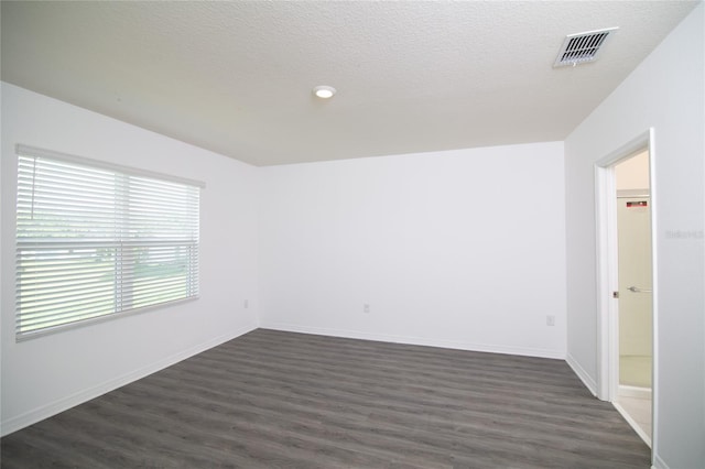 unfurnished room with visible vents, a textured ceiling, and dark wood-type flooring