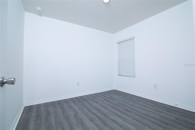 spare room featuring baseboards and dark wood-type flooring