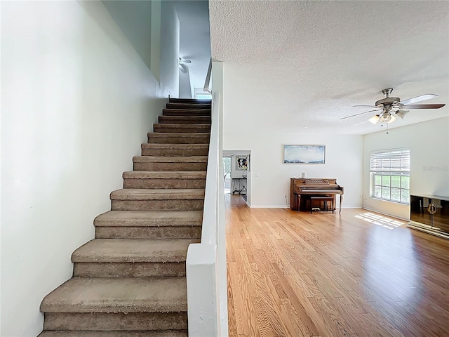 stairway featuring ceiling fan, baseboards, a textured ceiling, and wood finished floors