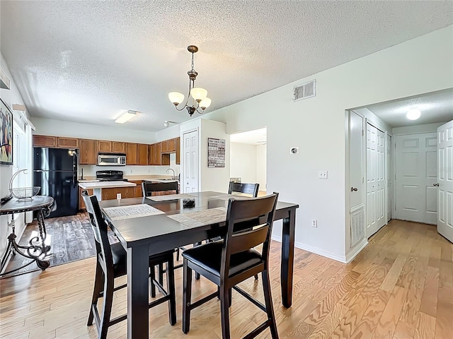 dining space with visible vents, baseboards, light wood-style floors, a notable chandelier, and a textured ceiling