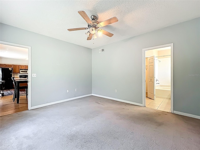 unfurnished bedroom featuring baseboards, visible vents, freestanding refrigerator, a textured ceiling, and light colored carpet