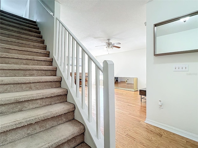 staircase with ceiling fan, baseboards, a textured ceiling, and wood finished floors