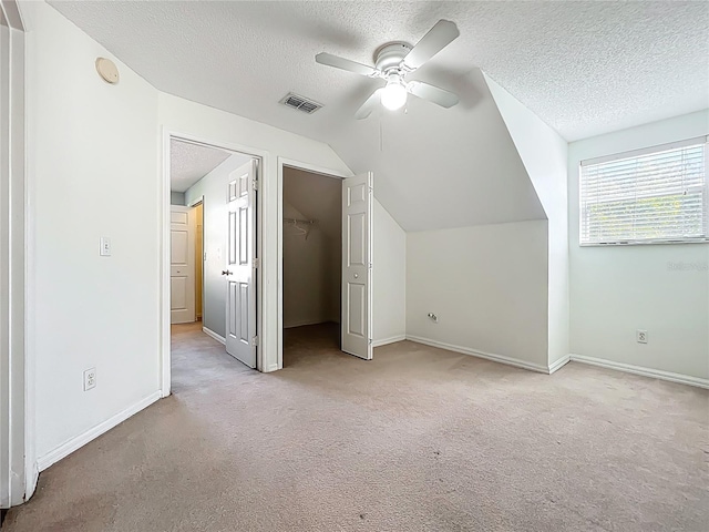 additional living space with visible vents, carpet, vaulted ceiling, a textured ceiling, and a ceiling fan