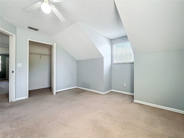 additional living space featuring visible vents, a textured ceiling, carpet flooring, and vaulted ceiling