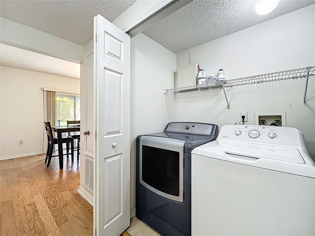 washroom with baseboards, light wood finished floors, laundry area, a textured ceiling, and washer and clothes dryer