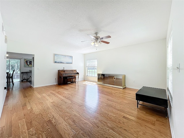 misc room with baseboards, light wood-style flooring, a textured ceiling, and ceiling fan